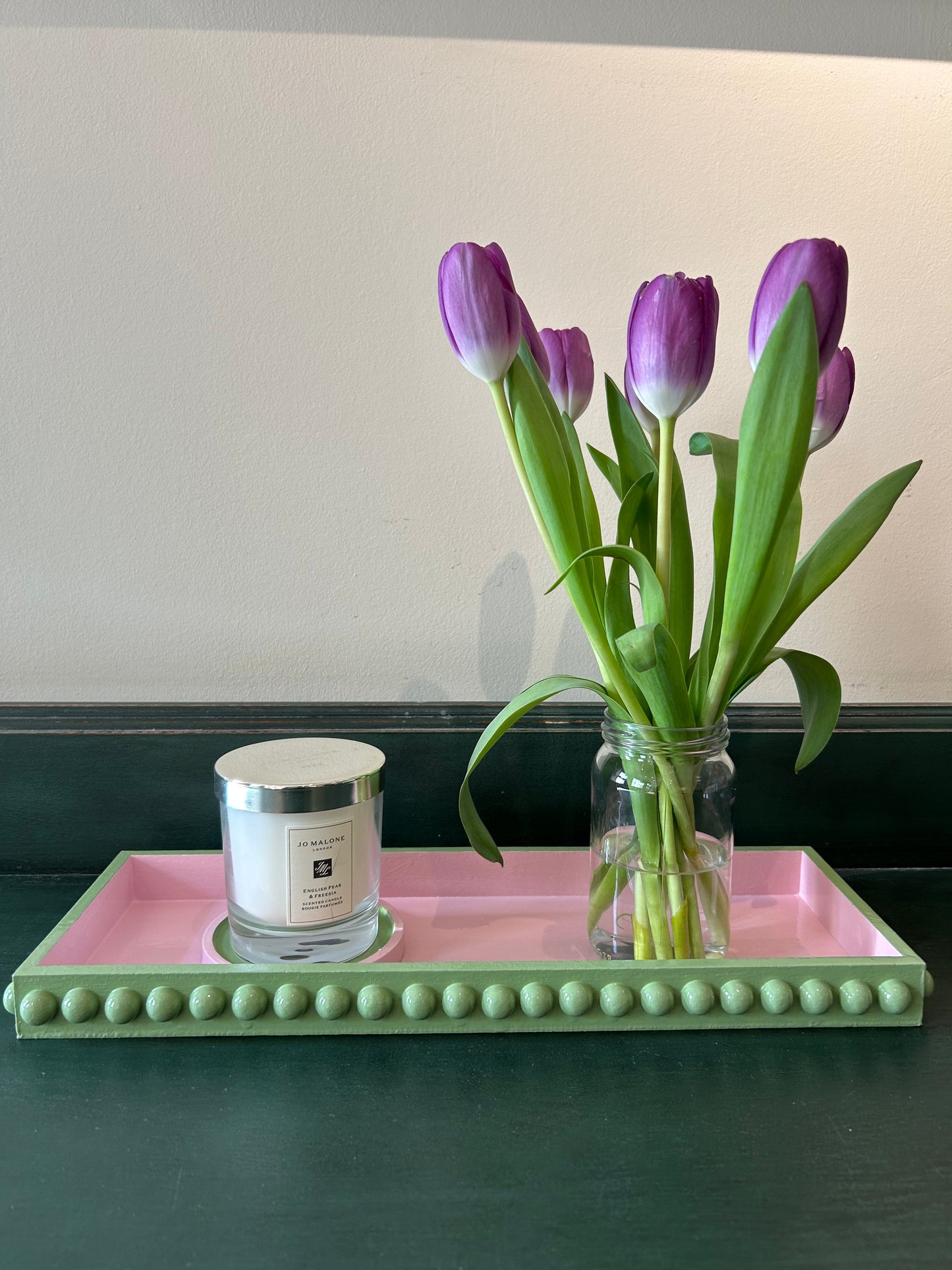 A hand painted green and pink bobbin style tray with gloss finish, displayed on a flat surface with a candle and a vase of tulips placed on it.