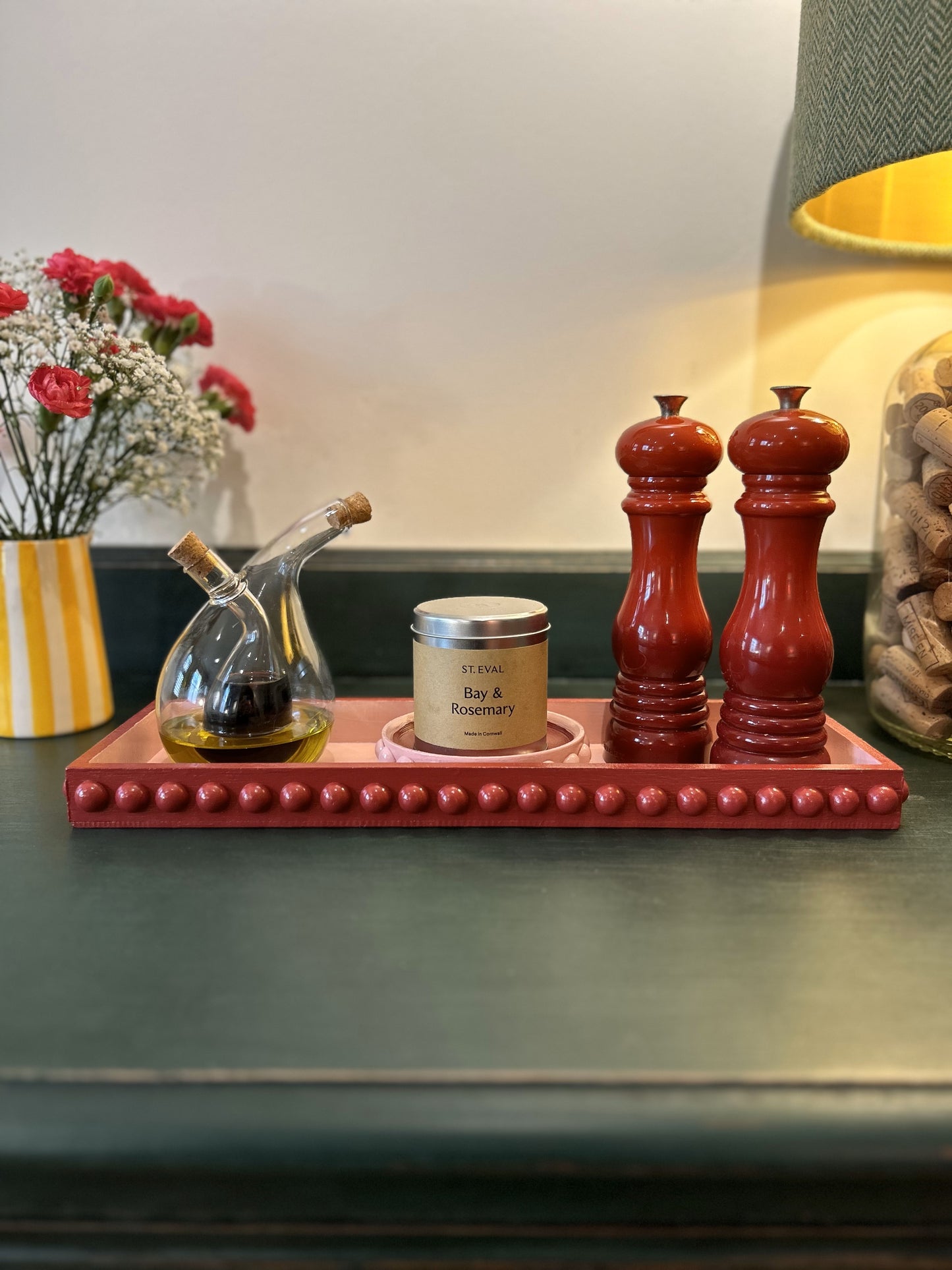 A hand painted red and pink bobbin style decorative tray on a table, adorned with a gloss finish and surrounded by a salt shaker, pepper shaker, and a small candle.