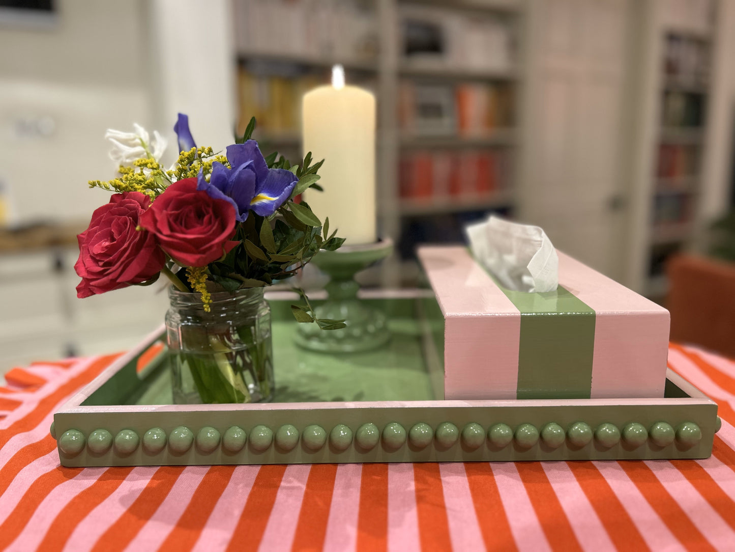 A hand painted green coffee table tray with wooden bobbins and a pink edge, displayed on a table with a striped tablecloth.