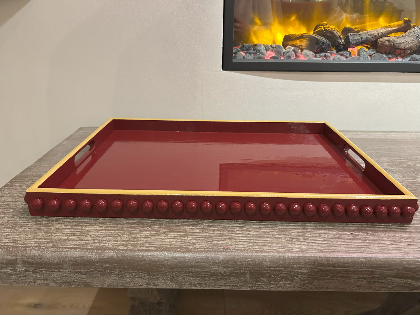 A rectangular, hand painted deep red coffee table tray with mustard yellow edge and handles.