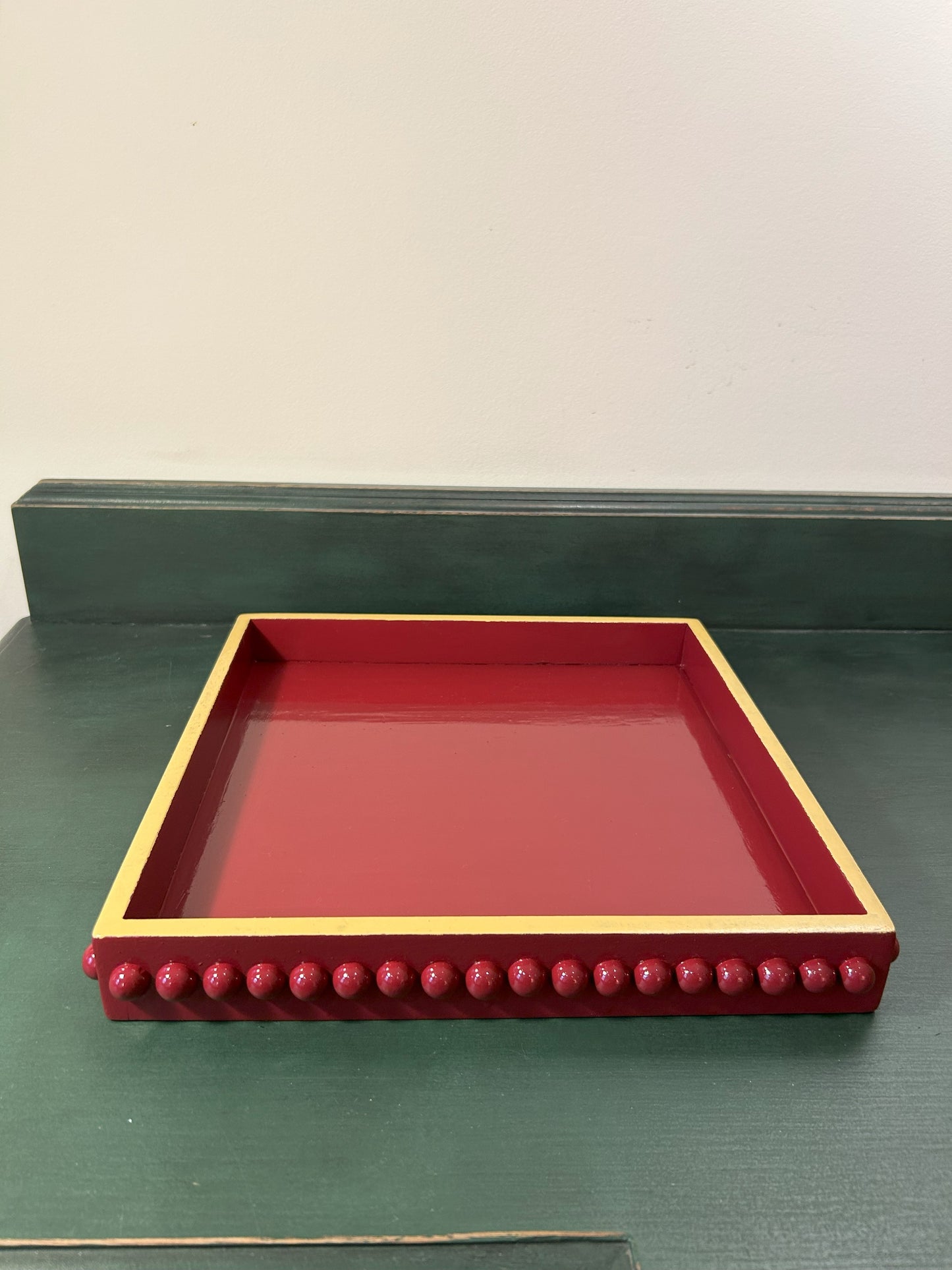 A hand painted square decorative coffee table tray with a dark red bobbin style pattern and mustard edge, gloss finish.