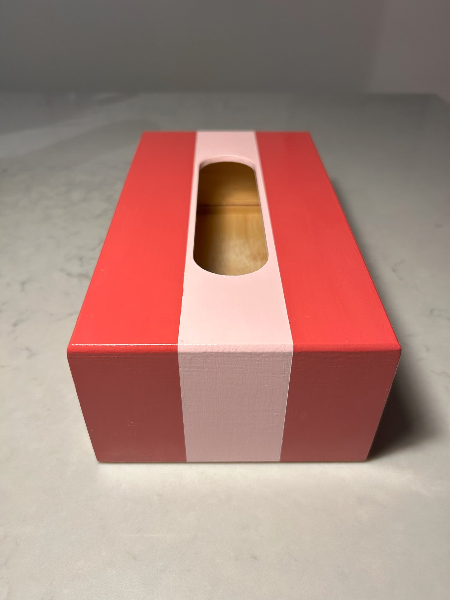 A hand painted red and pink striped tissue box on a table with a vase of tulips and a candle in the background.