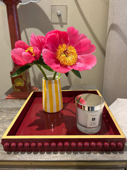 Hand-painted red and mustard yellow bobbin style decorative tray styled on a bedside table with candles, fresh flowers and decorative accessories.