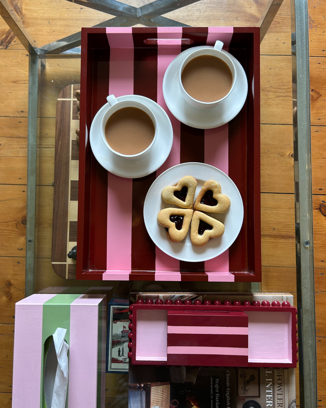Hand-painted pink and red striped decorative tray with handles styled on a coffee table with tea, biscuits and colourful home accessories.