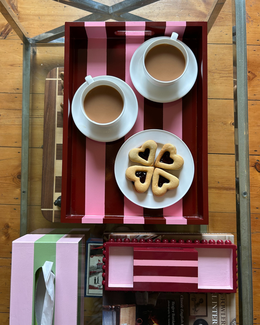 Hand-painted pink and red striped decorative tray with handles styled on a coffee table with tea, biscuits and colourful home accessories.