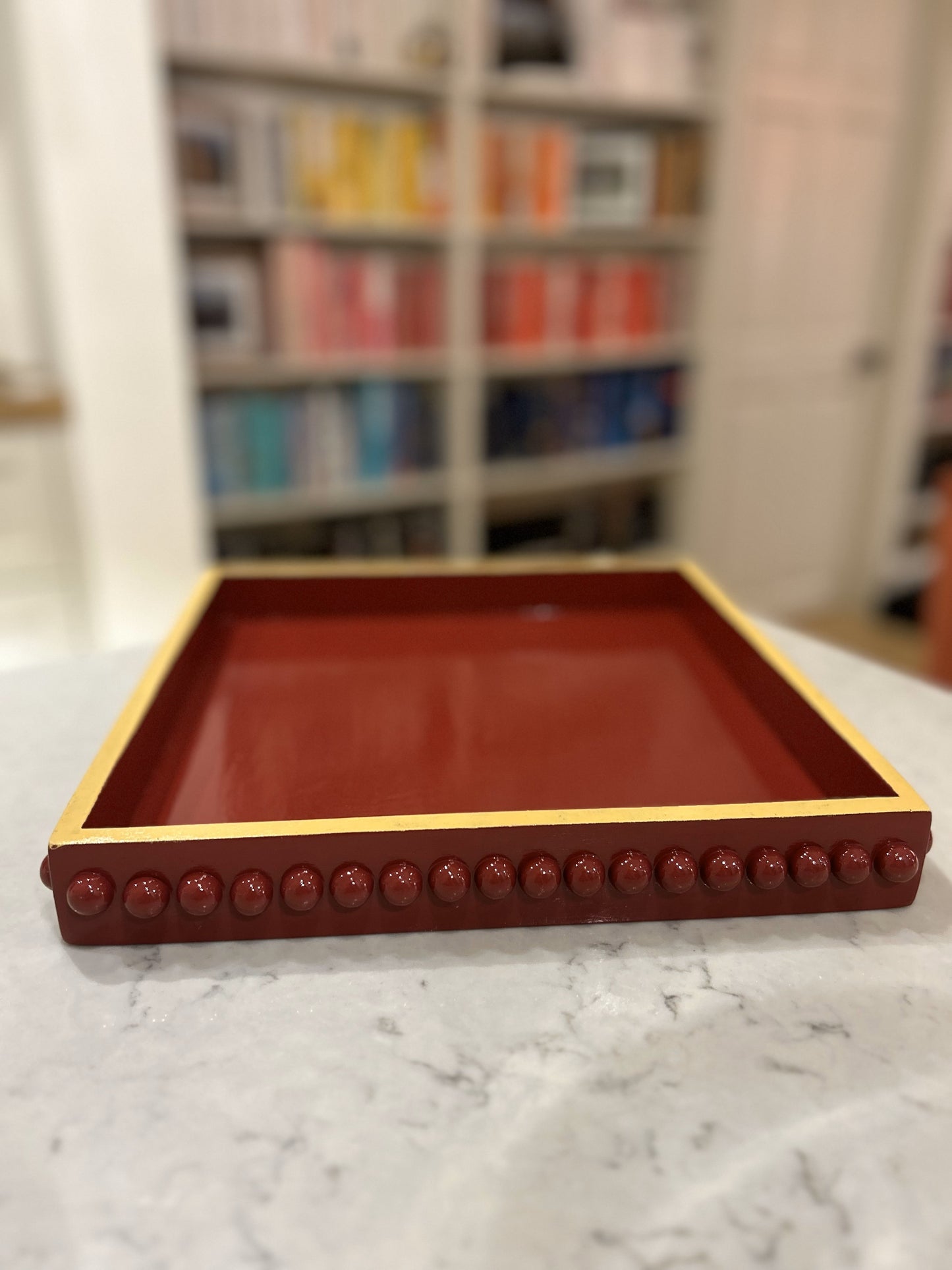 A hand painted square decorative coffee table tray with a dark red bobbin style pattern and mustard edge, gloss finish. 