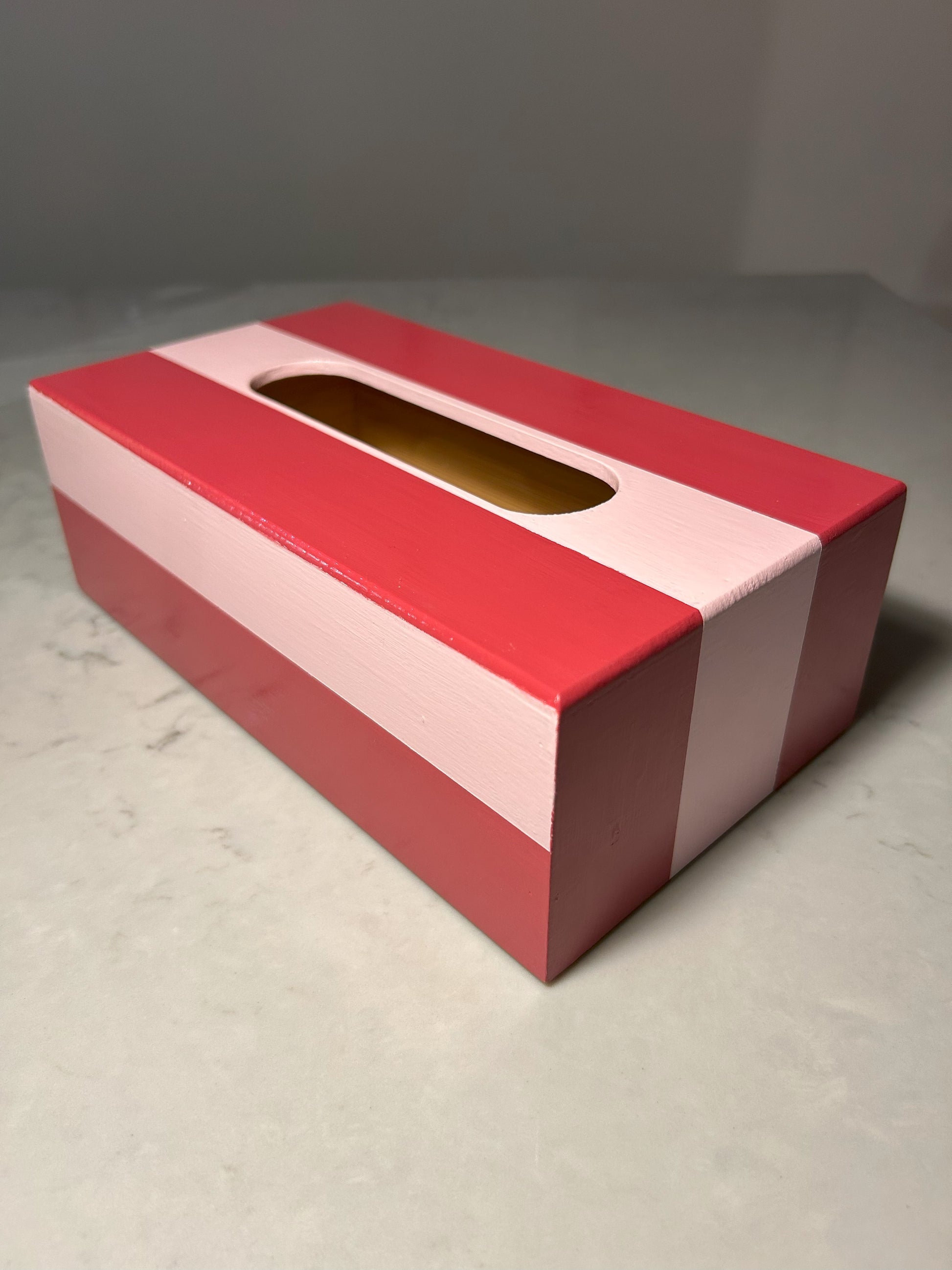 A hand painted red and pink striped tissue box on a table.